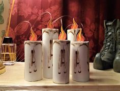 four white candles sitting on top of a wooden table next to boots and vases