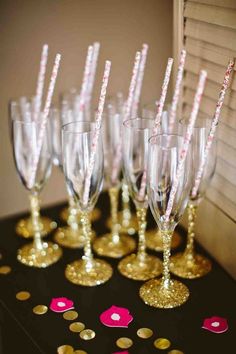 champagne flutes lined up on a table with confetti sticks in the middle and gold rimmed glasses