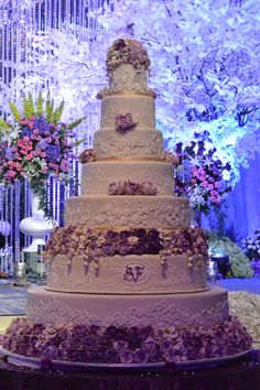 a large wedding cake with purple flowers on the top and bottom tier is displayed in front of an elaborately decorated backdrop