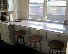 three stools are sitting in front of the counter top near two windows and a microwave