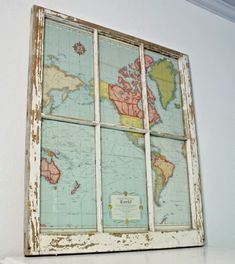 an old window with a world map on the glass in front of it, sitting on a shelf next to a white wall