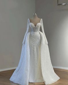 a white wedding dress with long sleeves and a cape on display in a museum room