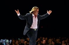 a man in a suit and tie walking on a runway with his arms out to the side