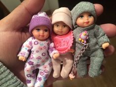 three little dolls are posed in the palm of someone's hand while wearing winter clothes