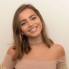 a woman with long hair wearing a tan top and smiling in front of a white wall