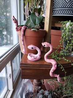 two pink snakes sitting on top of a wooden table next to a potted plant