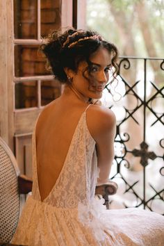 a woman in a white dress sitting on a chair looking off into the distance with her back to the camera