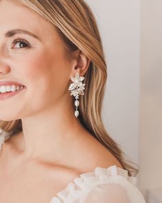 a woman in a white dress is smiling at the camera and wearing earrings with flowers on them