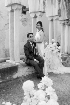 a man and woman sitting next to each other in front of some pillars with flowers