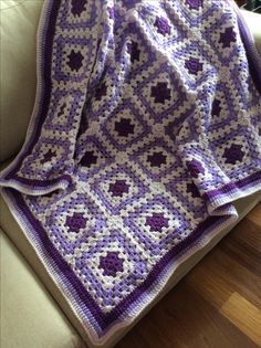 a purple and white crocheted blanket sitting on top of a couch