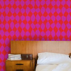 a bed sitting next to a pink wall with red and purple designs on the walls