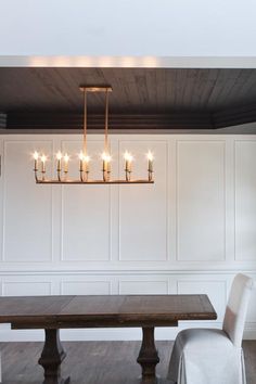 a dining room table and chairs with candles hanging from the chandelier above it