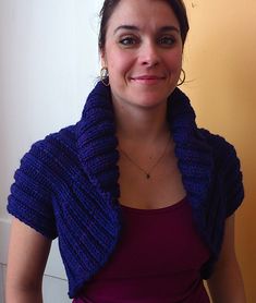 a woman wearing a purple shirt and blue knitted scarf around her neck smiling at the camera