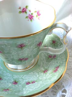 an antique tea cup and saucer with pink flowers on green, gold trimmings