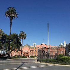 an empty street in front of a large building with palm trees on both sides and blue sky above