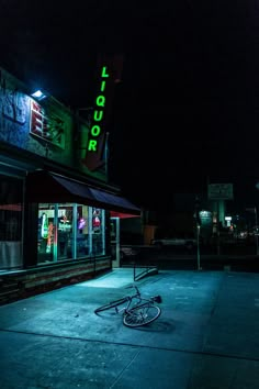 a bike is parked in front of a liquor store at night with neon lights on the building