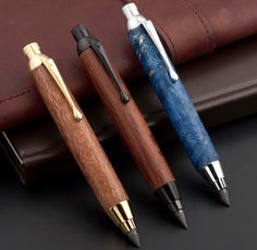 three different types of pens sitting next to each other on a black surface with a brown leather case