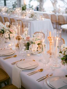 the table is set with white flowers and gold place settings, candles and napkins