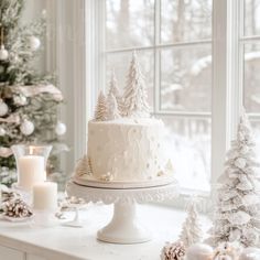 a white cake sitting on top of a table next to a christmas tree