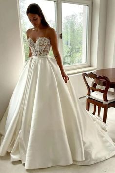 a woman standing in front of a window wearing a white wedding dress with flowers on it