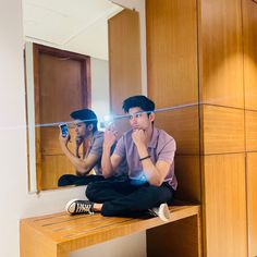 two men sitting on a wooden bench in front of a mirror with their cell phones