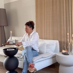 a woman sitting on a white couch next to a table with candles and vases