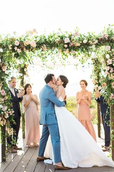 a bride and groom kissing in front of their wedding party at the end of an outdoor ceremony