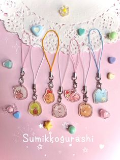 a bunch of key chains hanging on a pink background with the words sumikogurashi written below them