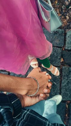 two people are holding hands and one is wearing a pink dress while the other holds a green purse