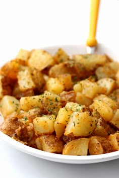 a white bowl filled with potatoes covered in seasoning next to a yellow handled fork