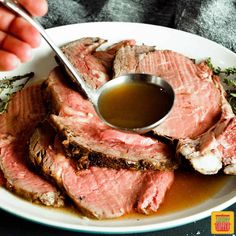 a person is dipping sauce on top of some meat in a white bowl with green herbs