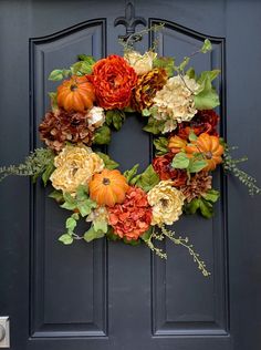 a wreath with flowers and leaves is hanging on the front door's black door