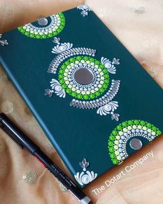 a green notebook with an eye design on it and a black pen next to it