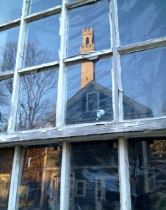 a clock tower seen through the window of an old building with glass panes on it