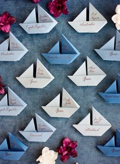 paper boats with names on them sitting next to pink flowers and white orchids in front of a blue background