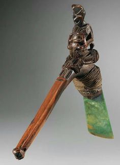 a metal object with a wooden handle holding a green stone and a large knife blade