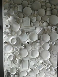 there are many white dishes and cups on the wall in this room, all stacked together