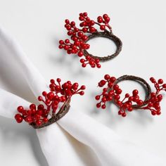 two napkin rings with red berries on them sitting next to a white cloth covered napkin