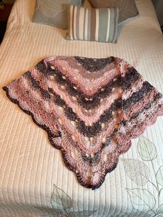 a crocheted shawl on top of a bed with pillows and pillow cases