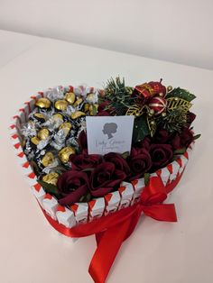 a heart - shaped box filled with chocolates and roses on a white table top