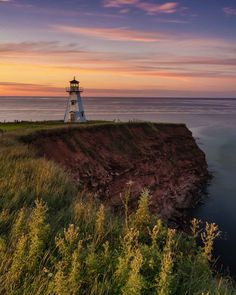 a light house sitting on top of a cliff next to the ocean under a colorful sky