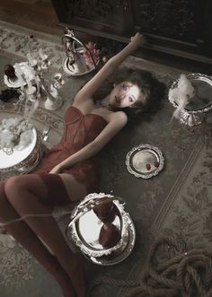 a woman laying on the floor in front of silver plates and dishes with her arms stretched out