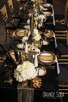 a long table is set with black and gold plates, napkins, and flowers