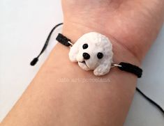 a small white dog beaded on a black string bracelet with beads around it's eyes