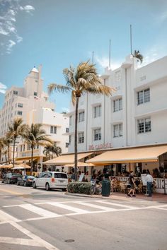 people are sitting at tables in front of a building with palm trees on the sidewalk