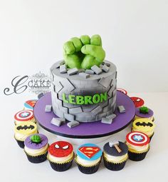 a birthday cake decorated with cupcakes and fondant superhero characters is displayed on a table