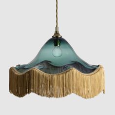 a green and gold hanging light with fringes on the bottom, in front of a gray background