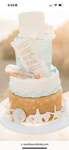 a three tiered cake sitting on top of a white plate covered in sand and seashells