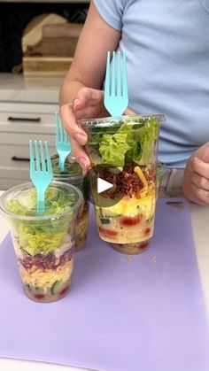 a person holding two plastic forks and cups with food in them on a purple mat