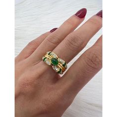 a woman's hand wearing a gold ring with green and white stones